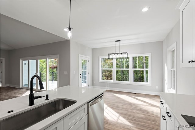 kitchen with pendant lighting, a sink, stainless steel dishwasher, white cabinetry, and light wood-style floors