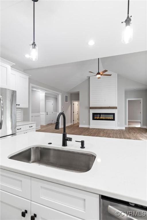 kitchen featuring open floor plan, light countertops, appliances with stainless steel finishes, a glass covered fireplace, and a sink