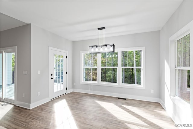 unfurnished dining area with a healthy amount of sunlight, an inviting chandelier, baseboards, and wood finished floors