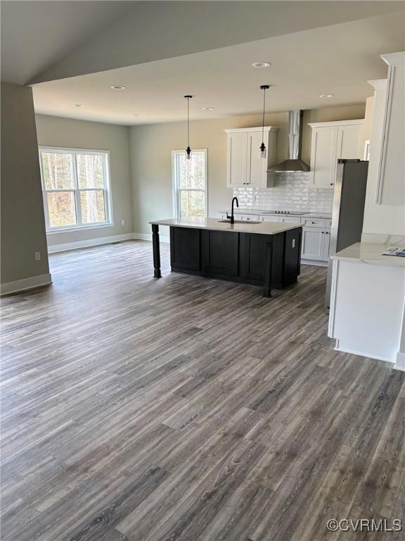 kitchen with a kitchen island with sink, a sink, wall chimney range hood, freestanding refrigerator, and light countertops