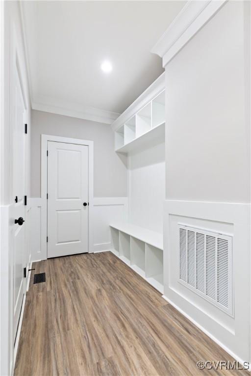 mudroom featuring a decorative wall, wood finished floors, visible vents, and ornamental molding