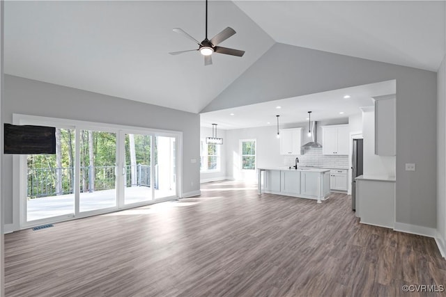 unfurnished living room featuring high vaulted ceiling, a ceiling fan, a sink, wood finished floors, and baseboards