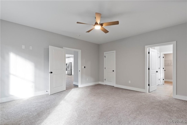 unfurnished bedroom featuring light colored carpet, freestanding refrigerator, baseboards, and ceiling fan