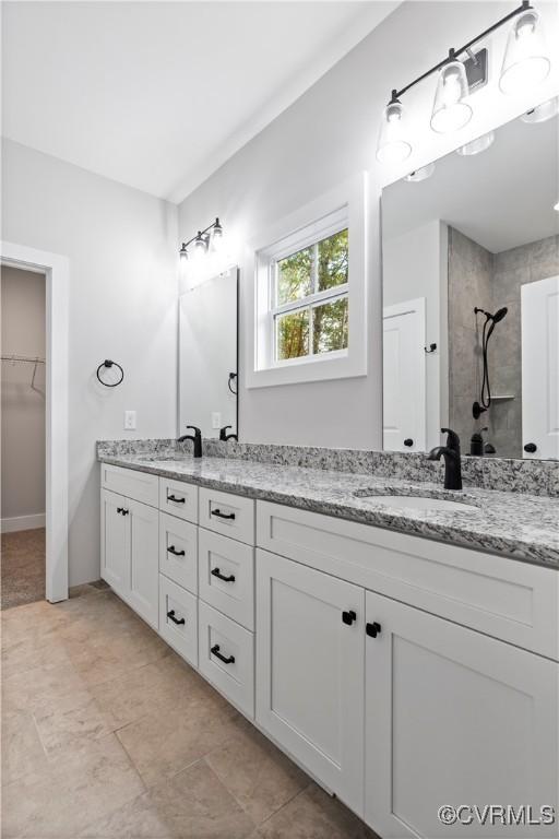 bathroom featuring double vanity, tiled shower, a walk in closet, and a sink