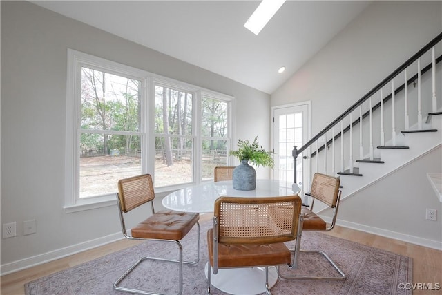 dining space with wood finished floors, recessed lighting, vaulted ceiling with skylight, baseboards, and stairs