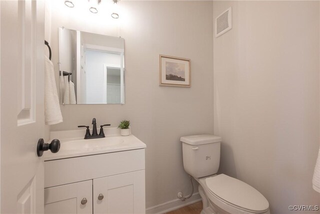 half bath with visible vents, baseboards, toilet, and vanity