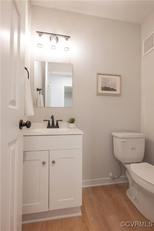 bathroom with vanity, wood finished floors, visible vents, baseboards, and toilet