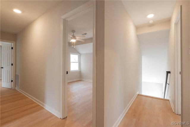 hall with visible vents, baseboards, lofted ceiling, and light wood-style flooring