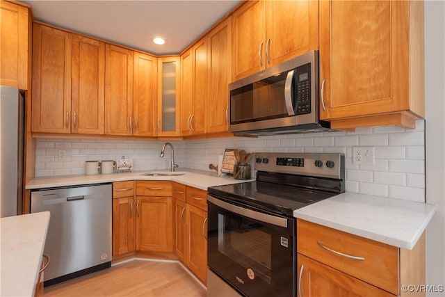 kitchen featuring glass insert cabinets, stainless steel appliances, light countertops, and a sink