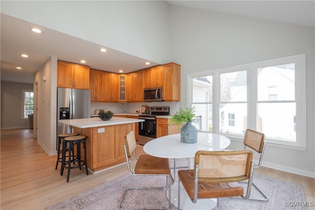 kitchen featuring a kitchen island, stainless steel appliances, a breakfast bar area, light countertops, and glass insert cabinets