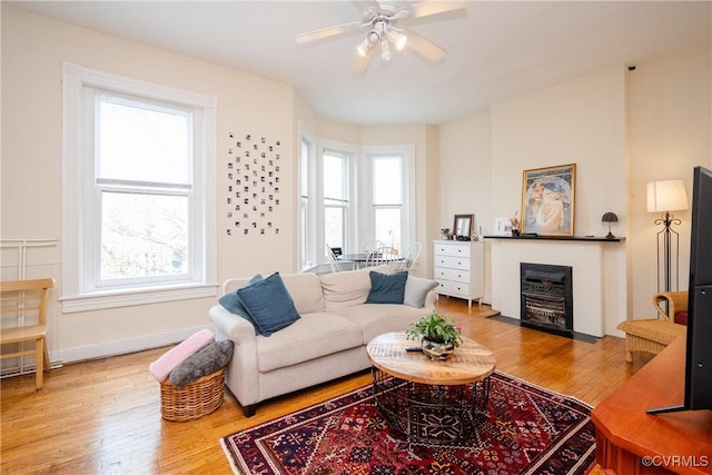 living room with a fireplace with flush hearth, baseboards, ceiling fan, and wood finished floors