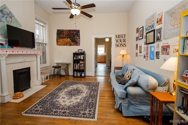 living area featuring a fireplace, wood finished floors, baseboards, and ceiling fan