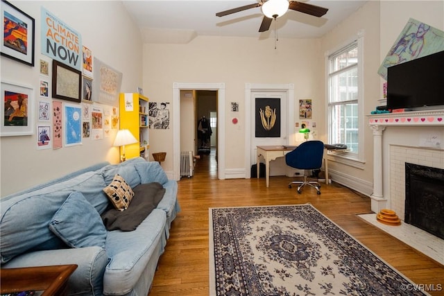 living room featuring baseboards, a brick fireplace, wood finished floors, and a ceiling fan