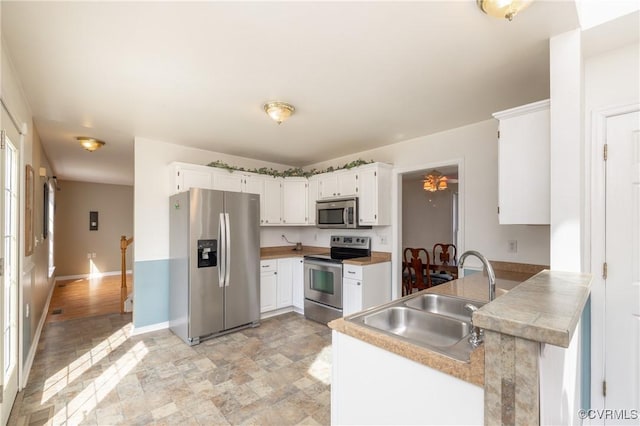 kitchen with a sink, baseboards, appliances with stainless steel finishes, and white cabinetry