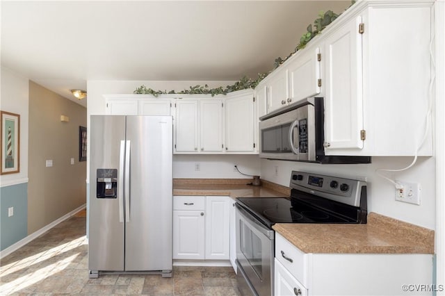 kitchen featuring baseboards, stainless steel appliances, light countertops, white cabinets, and stone finish floor