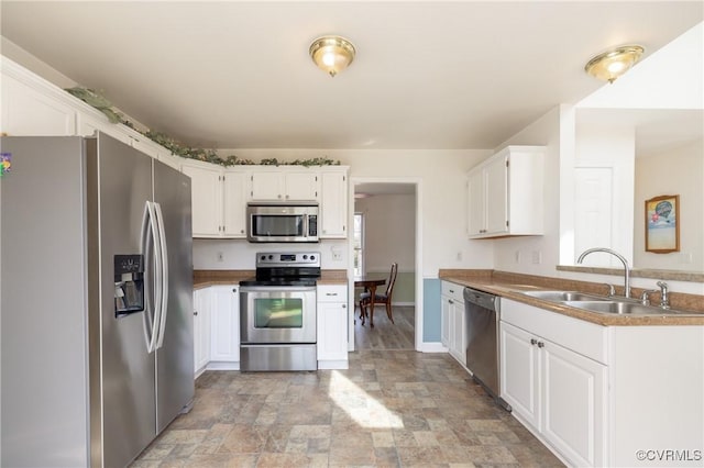 kitchen with white cabinets, stainless steel appliances, stone finish flooring, and a sink