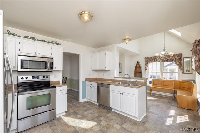 kitchen featuring a peninsula, a sink, stainless steel appliances, white cabinetry, and a notable chandelier