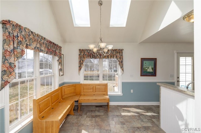 dining area with lofted ceiling with skylight, plenty of natural light, stone finish floor, and an inviting chandelier