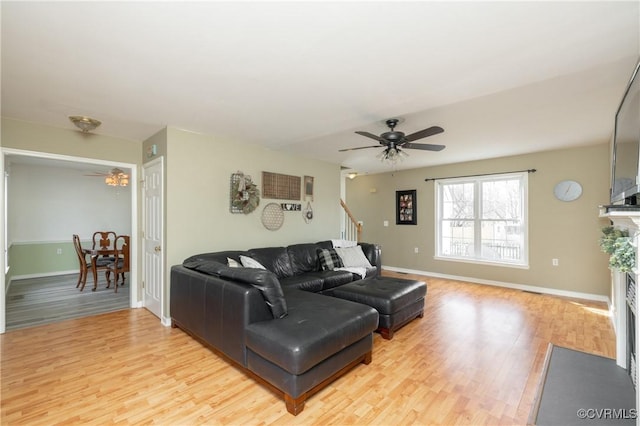 living area featuring a fireplace with flush hearth, baseboards, light wood finished floors, and ceiling fan