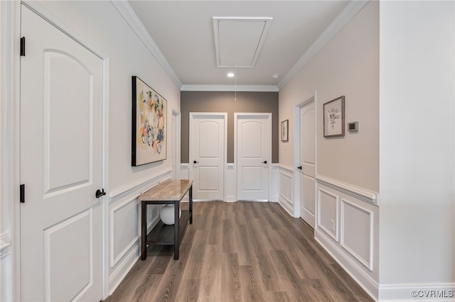 corridor featuring attic access, a decorative wall, wood finished floors, crown molding, and a wainscoted wall