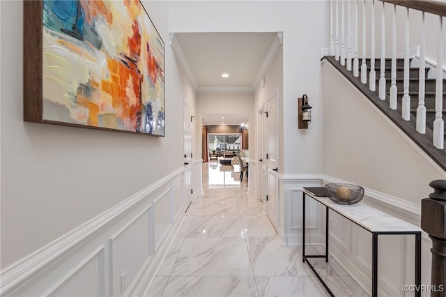 corridor with a decorative wall, crown molding, light marble finish floors, stairway, and a wainscoted wall