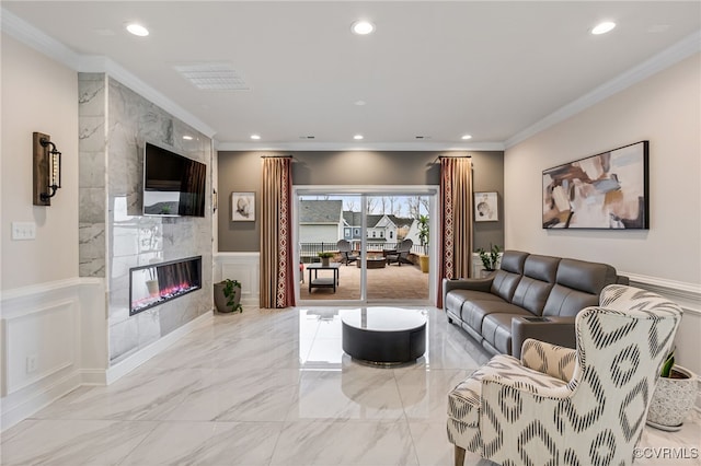 living room featuring crown molding, a premium fireplace, wainscoting, recessed lighting, and a decorative wall