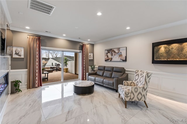 living room featuring a decorative wall, crown molding, recessed lighting, light marble finish floors, and a wainscoted wall