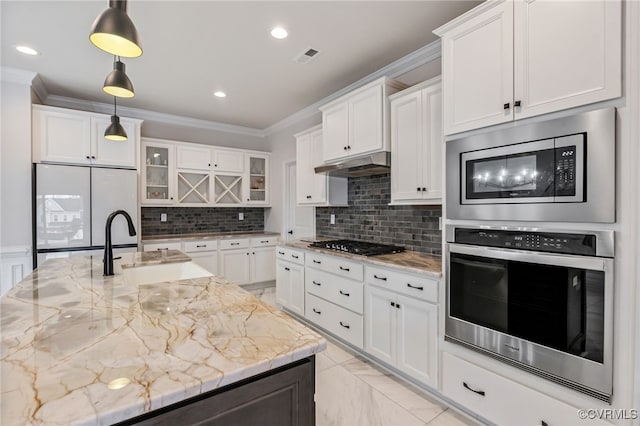 kitchen with stainless steel appliances, under cabinet range hood, a sink, crown molding, and white cabinetry