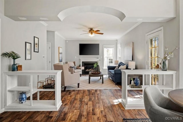 living room with ceiling fan, dark wood-type flooring, ornamental molding, and a fireplace