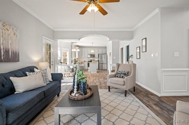 living area with ceiling fan, arched walkways, light wood-type flooring, and ornamental molding