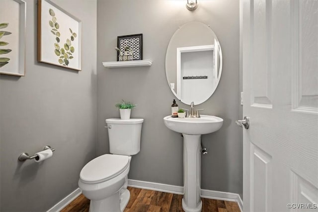 half bathroom with baseboards, toilet, and wood finished floors