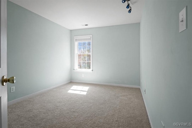 carpeted spare room with visible vents, rail lighting, and baseboards