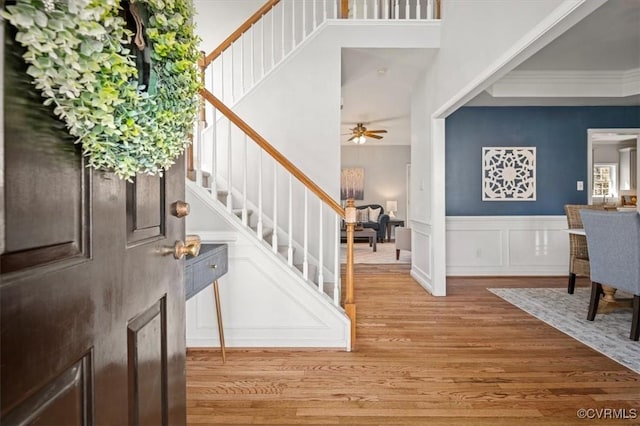 entrance foyer featuring wood finished floors, wainscoting, a decorative wall, ceiling fan, and stairs