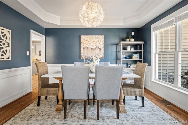 dining room featuring an inviting chandelier, a raised ceiling, wood finished floors, and a wainscoted wall