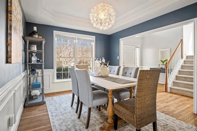 dining space featuring a wainscoted wall, stairway, a tray ceiling, wood finished floors, and a notable chandelier