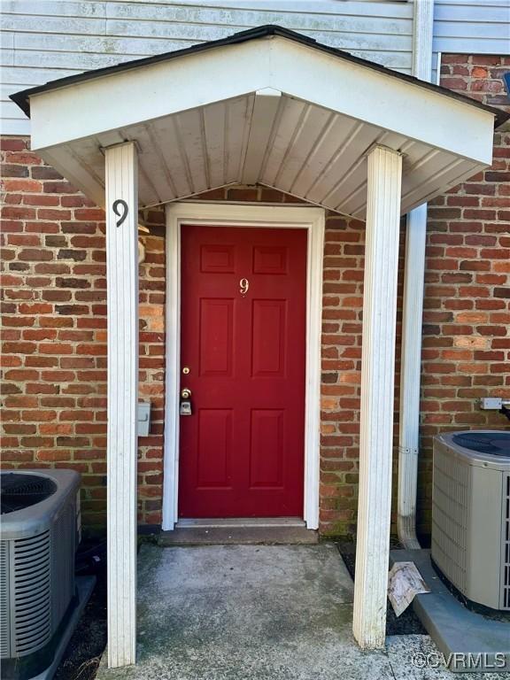 view of exterior entry with brick siding and central AC