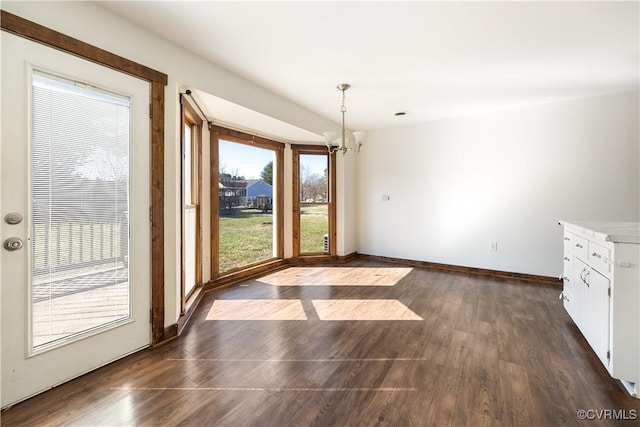 unfurnished dining area with a chandelier, baseboards, and dark wood-style flooring