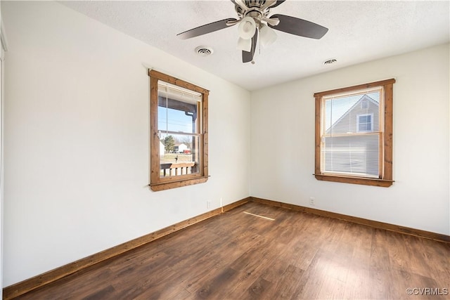 empty room with visible vents, plenty of natural light, dark wood-type flooring, and baseboards