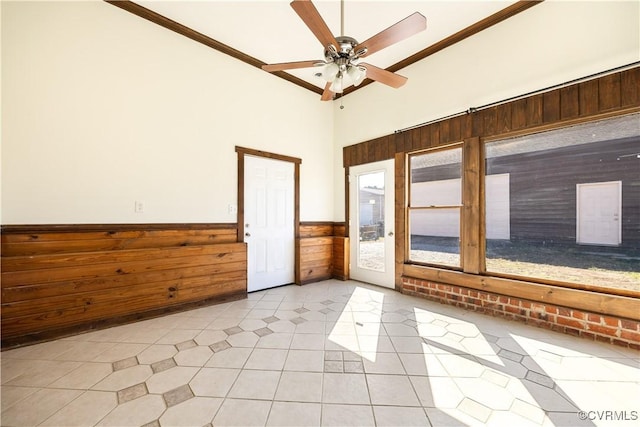 spare room with light tile patterned floors, a ceiling fan, a wainscoted wall, ornamental molding, and wood walls