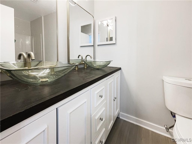 full bathroom with wood finished floors, baseboards, double vanity, a sink, and toilet