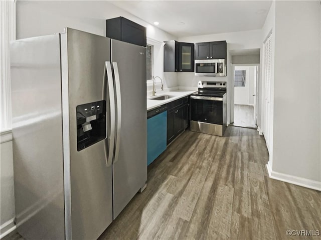 kitchen with glass insert cabinets, light countertops, appliances with stainless steel finishes, dark wood-style floors, and a sink