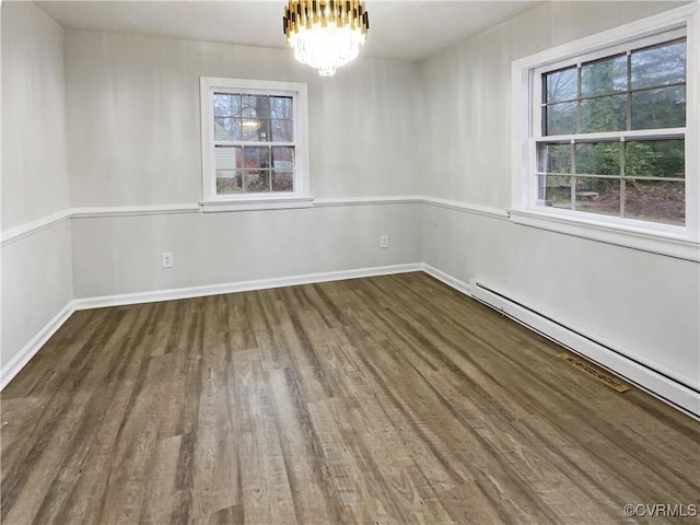 unfurnished room featuring a healthy amount of sunlight, wood finished floors, baseboard heating, and a chandelier