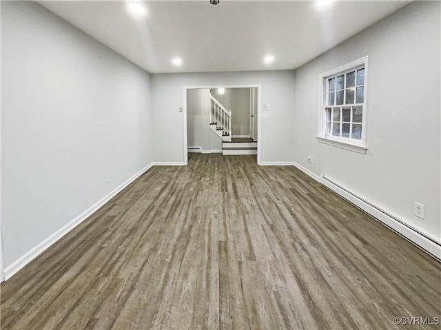 unfurnished room featuring a baseboard heating unit, stairs, wood finished floors, and baseboards