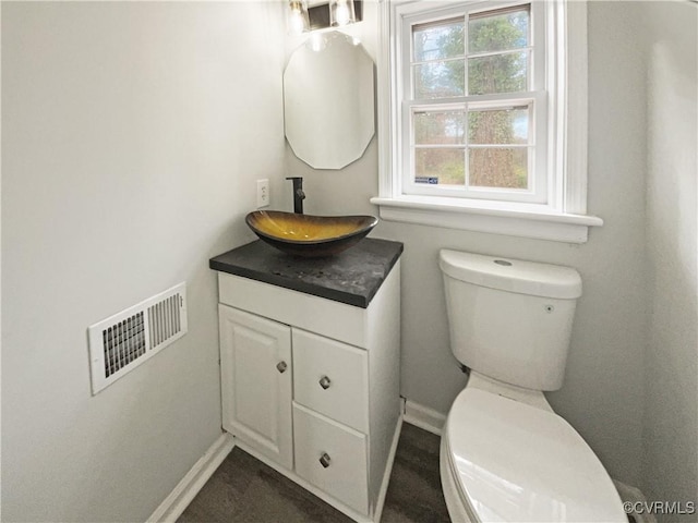 half bath with visible vents, baseboards, toilet, and vanity