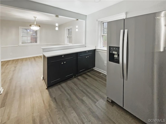 kitchen featuring dark cabinetry, wood finished floors, stainless steel fridge, and light countertops