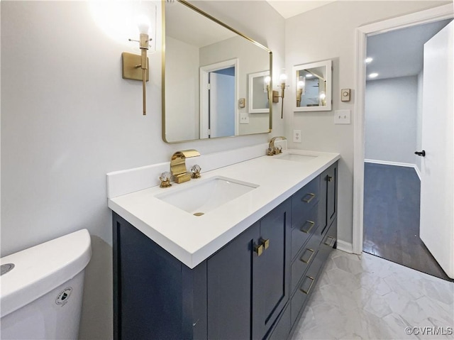 bathroom featuring a sink, toilet, marble finish floor, and double vanity