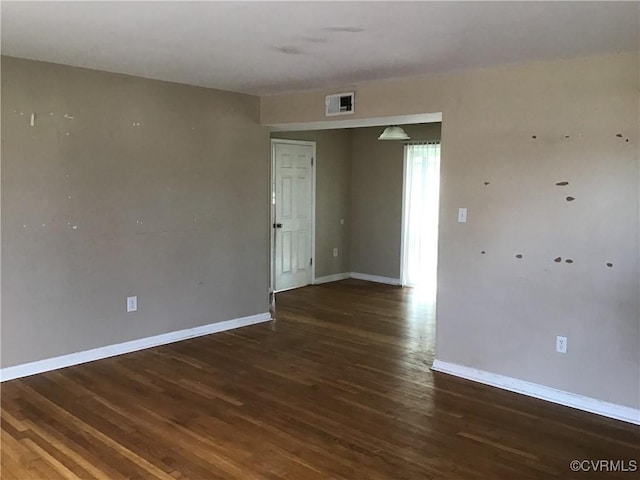 empty room featuring wood finished floors, visible vents, and baseboards