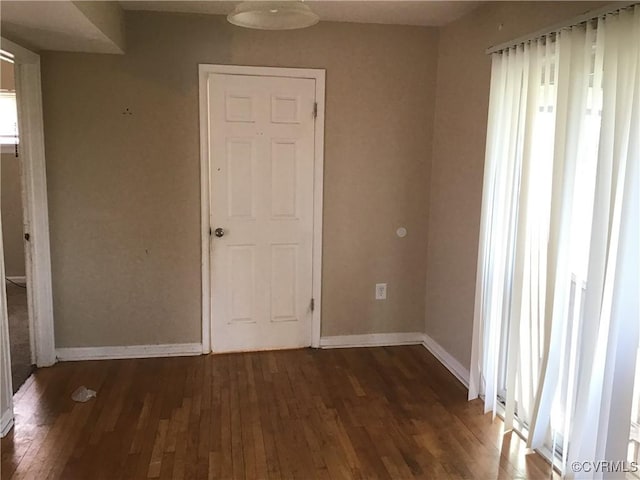 spare room with baseboards and dark wood-style flooring