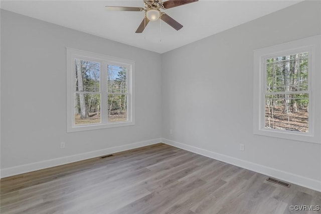 spare room featuring light wood finished floors, visible vents, a ceiling fan, and baseboards