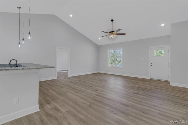 unfurnished living room featuring light wood-type flooring, baseboards, high vaulted ceiling, and a ceiling fan